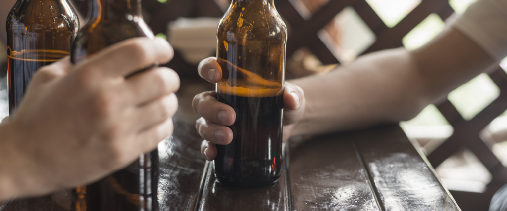 Mãos segurando garrafas de cerveja em uma mesa